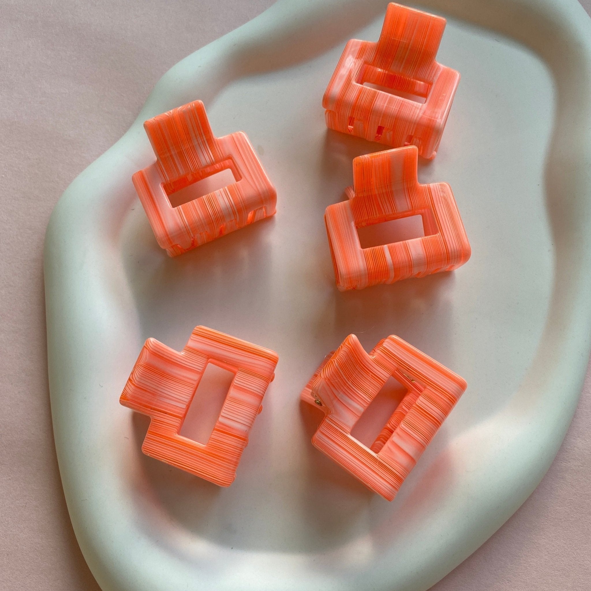 Mehrere kleine eckige Haarklammern in Neonorange liegen in weißer Schale.
