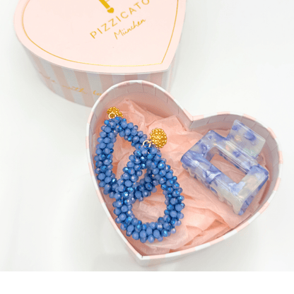 Geöffnete Pizzicato Herzgeschenkbox mit blauen Statement-Ohrringen und hellblauer Haarspange